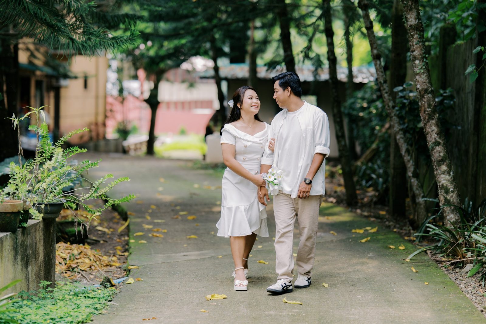 Arnaldo and Regine walking arm in arm along a tree-lined garden path