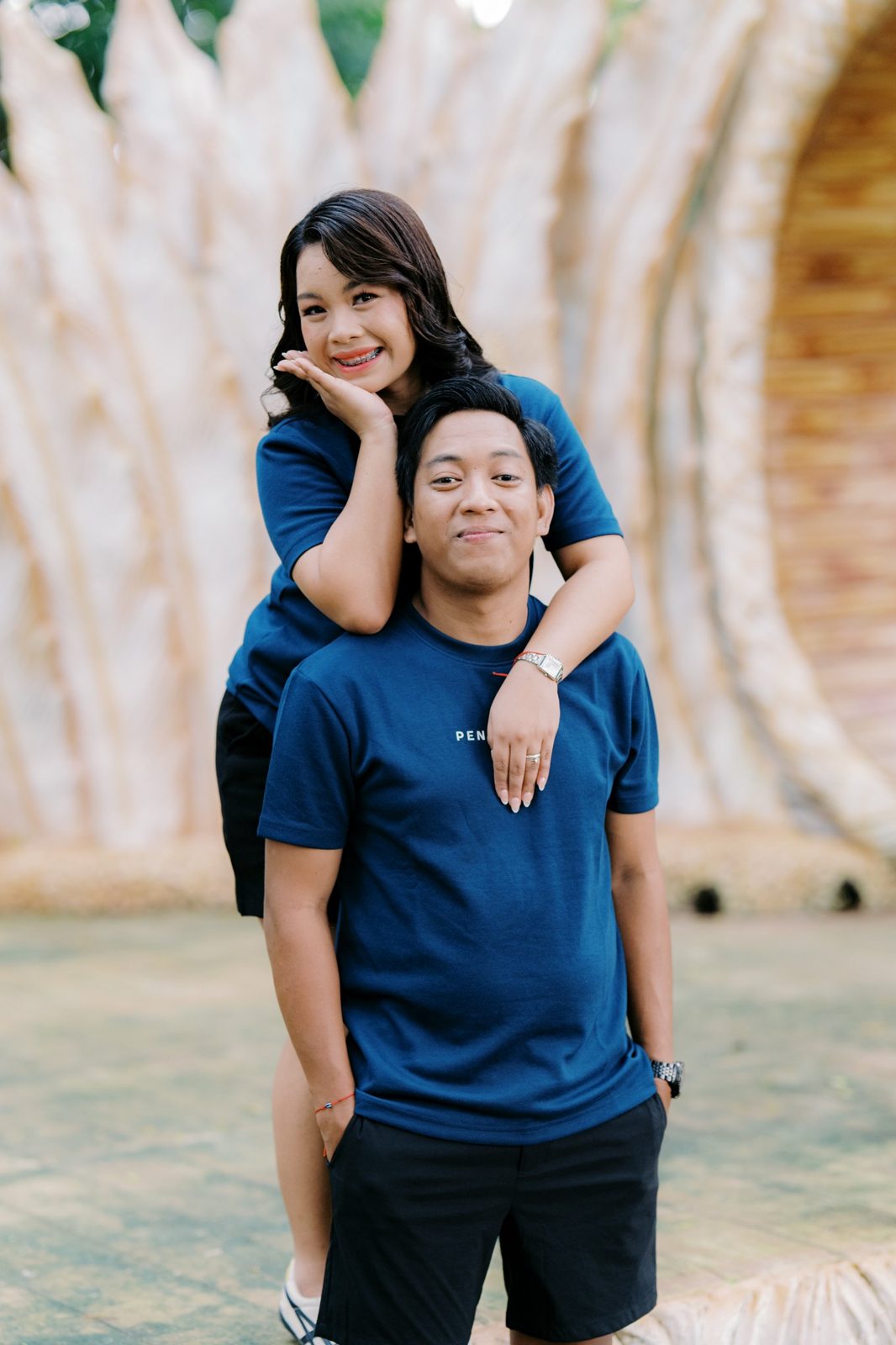 Regine leaning playfully over Arnaldo's shoulders, both in navy shirts